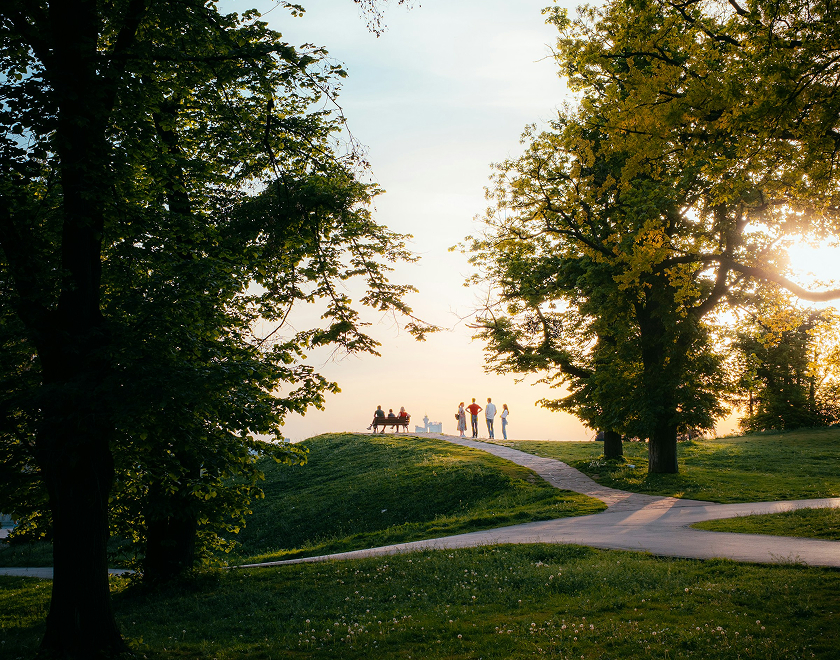 People walking along a path through a sunlit park at golden hour
